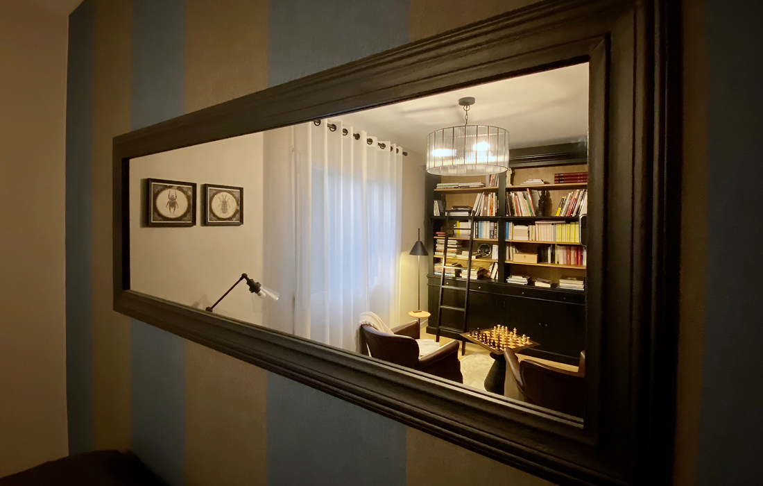 détail du miroir d'une bibliothèque et chambre d'amis décorée avec un bar des canapés club une echelle du papier peint en lin à rayures bleu et grises