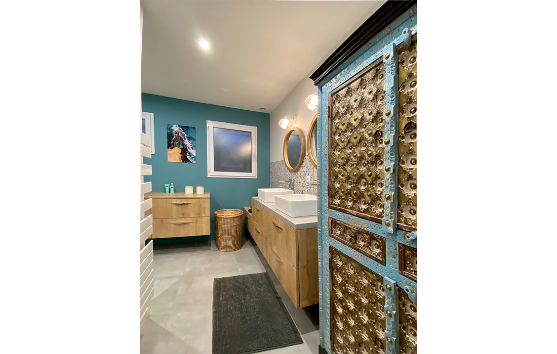détail du passage et de l'amoir de la salle de bain de la chambre exotique avec un carrelage en effet béton du terrazzo et des touches de bois et de peinture bleu
