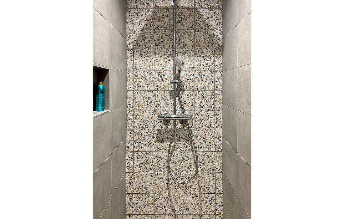 detail de la douche de la salle de bain de la chambre exotique avec un carrelage en effet béton du terrazzo et des touches de bois et de peinture bleu